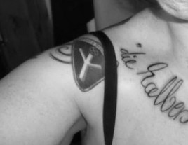 Szeen-Tattoos an der rechten Schulter von Katja Bütow:  Eine Lebensrune, darüber ein kleines gerundetets Hakenkreuz